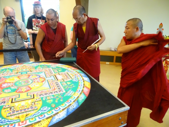 The monks scour the nearly finished mandala for finishing touches.